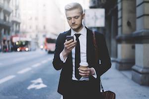 Young business man walking on street while checking his smart phone